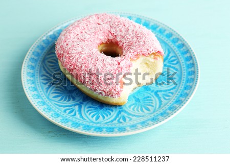 Bitten delicious donut on plate on wooden table close-up