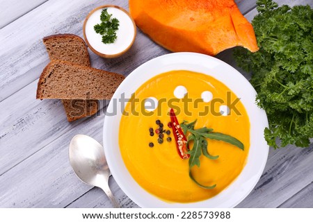 Pumpkin soup in white plate and pumpkin slice, bread, on wooden background