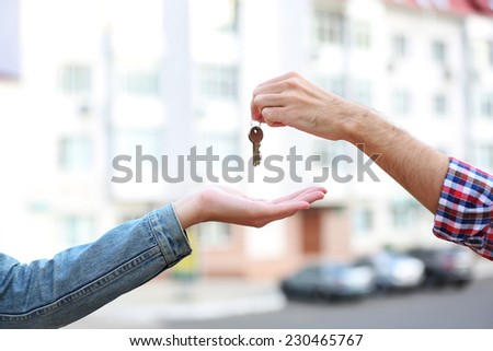 Man and woman hands hold keys near apartment house