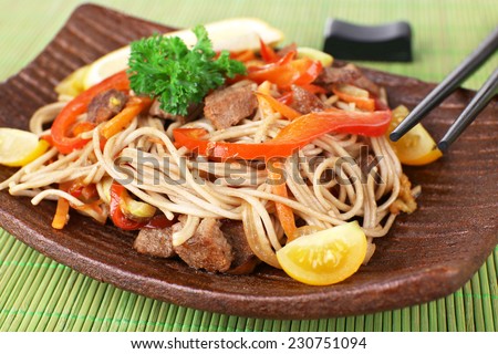 Chinese noodles with vegetables and roasted meat on plate on bamboo mat background