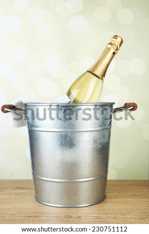 Bottle of champagne in metal ice bucket on wooden table on light background