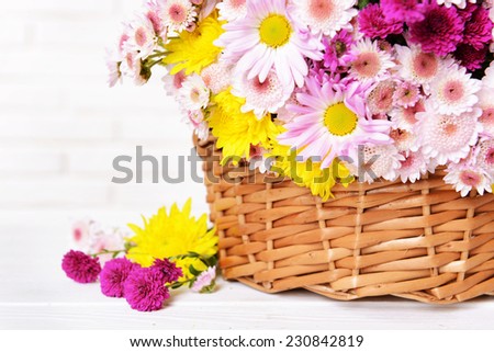 Beautiful flowers in wicker basket on table on light background