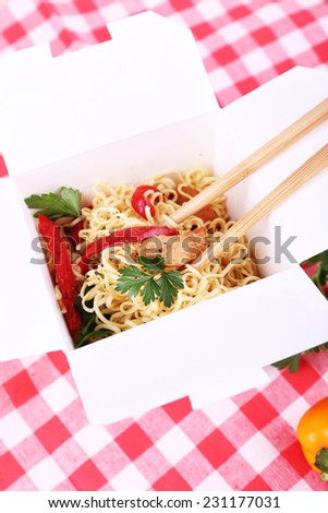 Chinese noodles and sticks in takeaway box on fabric background