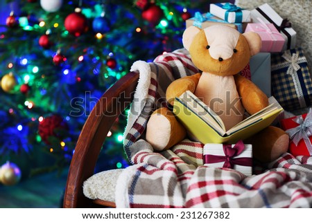 Teddy bear with book and gift boxes in rocking chair on Christmas tree background