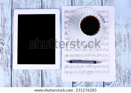 Tablet, cup of coffee printed music and earphones on wooden background