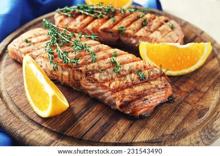 Grilled salmon  and orange slices on cutting board on wooden background