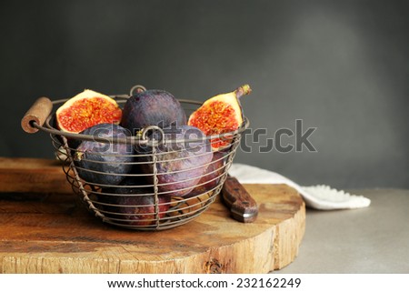 Ripe sweet figs in metal basket, on wooden table, on dark background