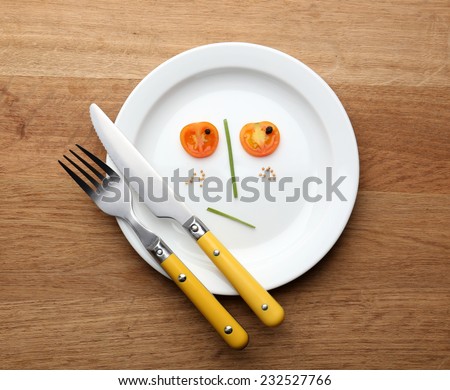 Vegetable face on plate with knife and fork on wooden table