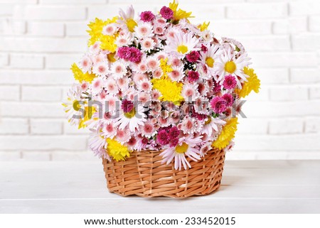 Beautiful flowers in wicker basket on table on light background