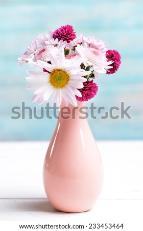 Beautiful flowers in vase on table on light blue background