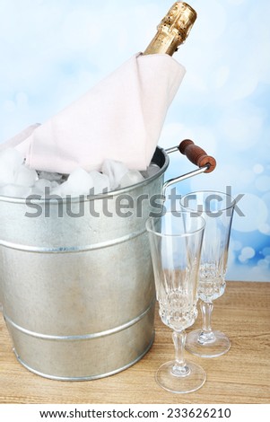 Bottle of champagne in metal ice bucket and two glasses on wooden table on light background