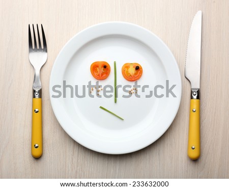 Vegetable face on plate with knife and fork on wooden table