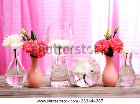 Beautiful flowers in vases on table on curtains background