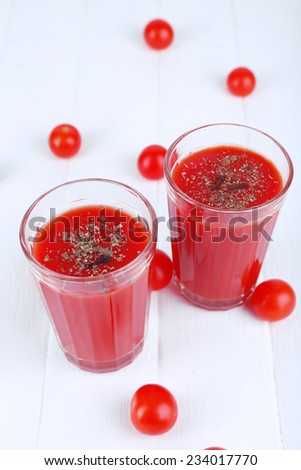 Tomato juice in glasses and fresh tomatoes on wooden background