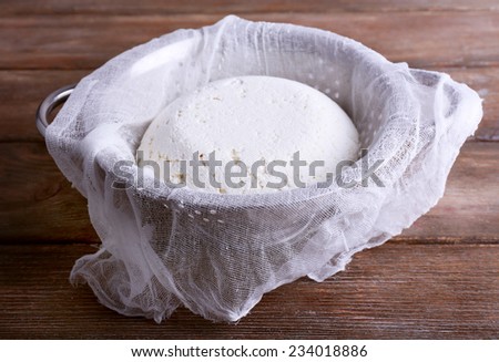 Cottage cheese on gauze in colander on wooden background