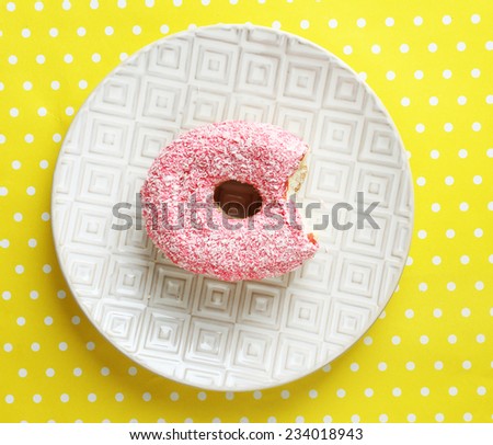 Bitten delicious donut on plate on colorful background