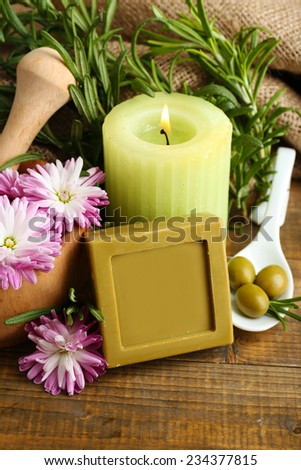 Handmade soap with the branches of rosemary on sackcloth, fresh flowers, olives and candle on wooden background