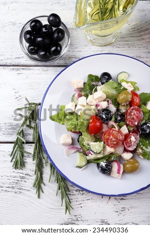 Plate of Greek salad served with olive oil and fresh olives on wooden background
