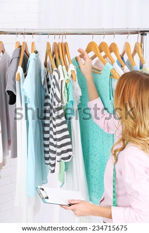 Beautiful young stylist near rack with hangers
