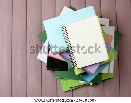 Notebook on top of pile of books and magazines on wooden background