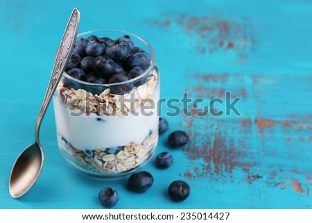 Healthy breakfast - yogurt with  blueberries and muesli served in glass jar, on color wooden background