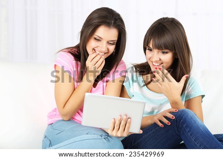 Beautiful girls twins with electronic tablet on sofa