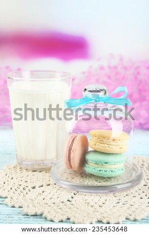 Gentle colorful macaroons in glass bell jar and milk glass on bright background