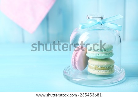 Gentle colorful macaroons in glass bell jar on color wooden table background