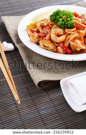 Chinese noodles with vegetables and seafood on plate on bamboo mat background