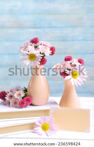 Beautiful flowers in vases on table on light blue background