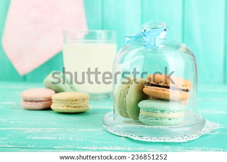 Gentle colorful macaroons in glass bell jar, milk glass and towel on color wooden table background