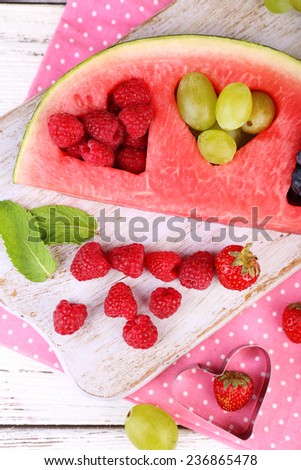 Fresh juicy watermelon slice  with cut out heart shape, filled fresh berries, on cutting board, on wooden background