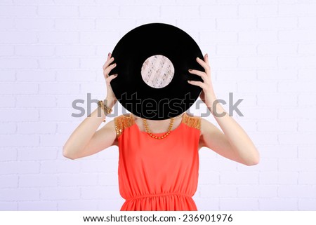 Young woman holding retro record in front of face, on shiny background