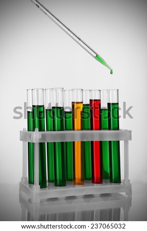 Pipette with drop of color liquid over container tubes on light background