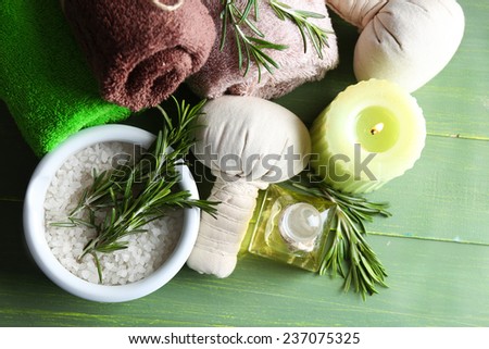Branches of rosemary and sea salt in bowl, towels, candle and bottle with massage oil on color wooden background. Rosemary spa concept