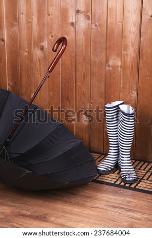Dirty wellington boots with umbrella on door mat in room