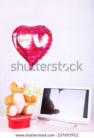 Teddy bear with present box, tree and love heart balloon on wooden  computer table, on the brick wall background