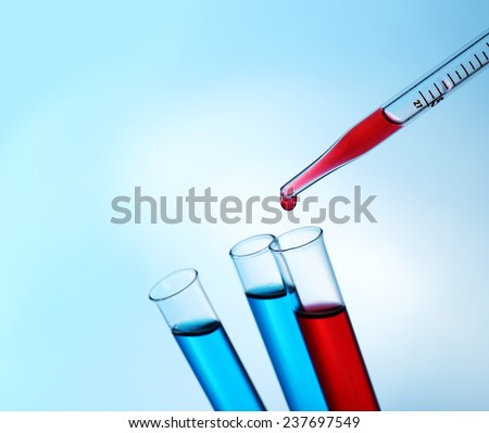 Pipette adding red fluid to the one of test-tubes on light background
