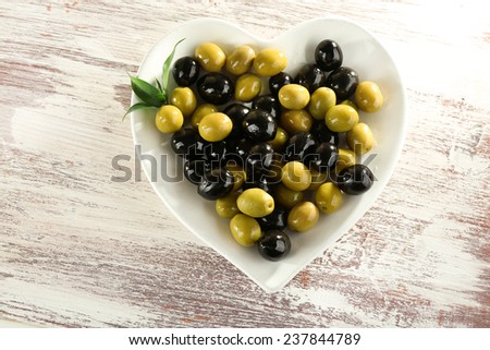 Plate in the form of heart with black and green olives on painted wooden background