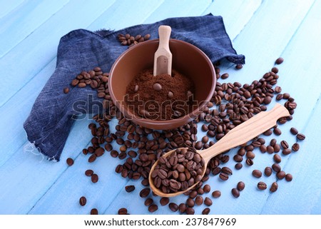Brown bowl of ground coffee and coffee beans with wooden spoon and scoop on blue wooden background with jeans material