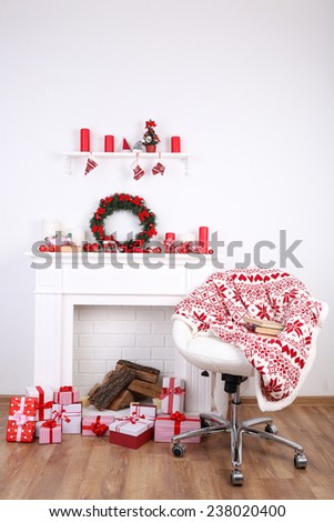 Chair near the Christmas fireplace with firewood and present boxes on wooden floor and white wall background