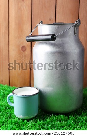 Retro can for milk and mug with milk  on green grass, on wooden background