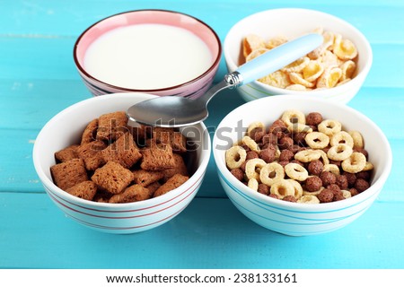 Various sweet cereals in ceramic bowls and bowl with milk on color wooden background