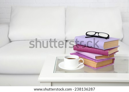 Purple books with cup and glasses on the tabletop on sofa background