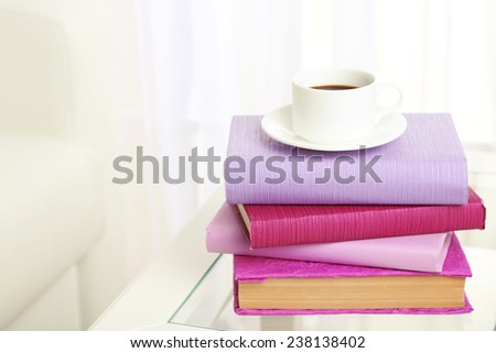 Purple books with cup near sofa on tabletop on the light window background