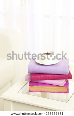 Purple books with cup near sofa on tabletop on the light window background