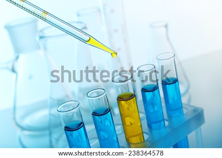 Pipette adding yellow fluid to one of several test-tubes with flasks on light background