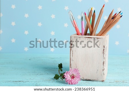 Different pens and pencils near flower on color wooden table on color wooden table and blue background with printed stars