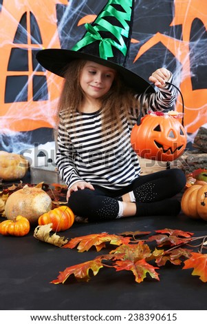 Little girl in hat asks candy on Halloween decorations background