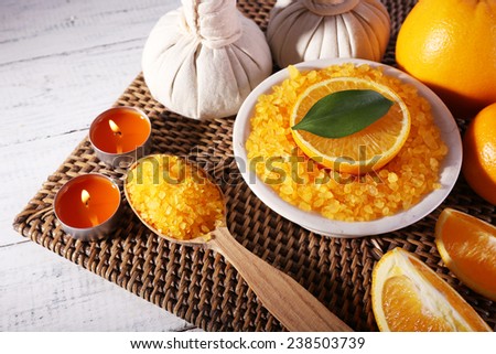 Accessories for massage therapy with candle light, spoon and bowl of bath salt on wicker mat, on color wooden background